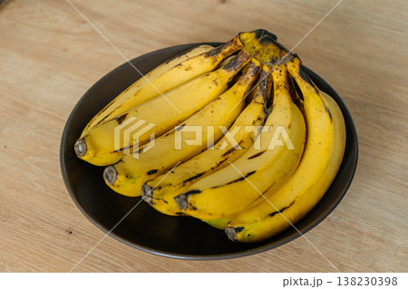 Vivid Scene Of Ripe Banana Cluster Placed On Wooden Surface In Cozy Kitchen Ambiance Vivid Scene Of Ripe Banana Cluster Placed On Wooden Surface In Cozy Kitchen Ambiance 138230398