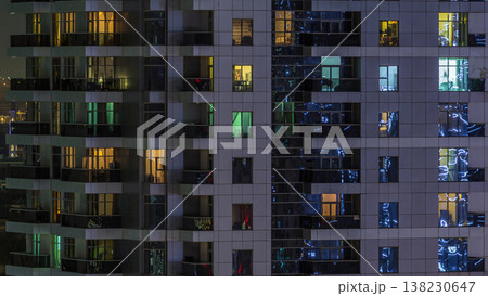 Rows of glowing windows with people in apartment building at night. 138230647