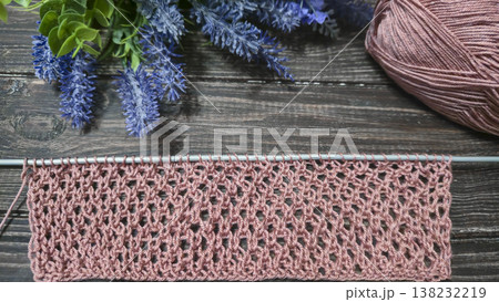 A relief openwork pattern knitted with colored yarn on a wooden background A relief openwork pattern knitted with colored yarn on a wooden background 138232219