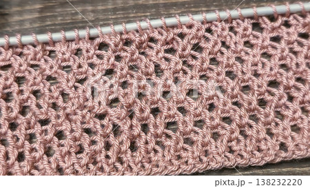 A relief openwork pattern knitted with colored yarn on a wooden background A relief openwork pattern knitted with colored yarn on a wooden background 138232220