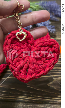 Red knitted heart-shaped keychain on a wooden background. Handmade. Red knitted heart-shaped keychain on a wooden background. Handmade. 138232241