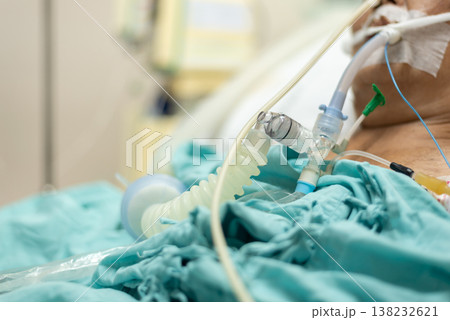 patient connected to ventilator in hospital bed receiving respiratory support critical care treatment equipment and tubing closeup healthcare environment 138232621