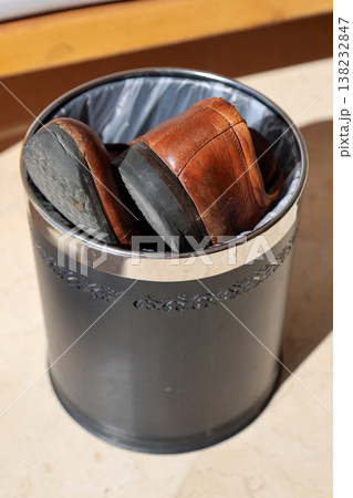 Old leather men's shoes discarded in a trash bin, symbolizing wear and tear, and the passage of time, reflecting on the journey of life and fashion 138232847