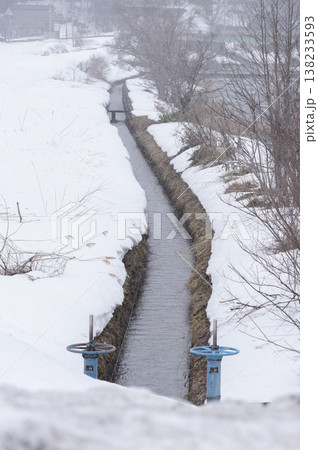 残雪の中を流れる農業用水路と青い水門の風景 残雪の中を流れる農業用水路と青い水門の風景 138233593