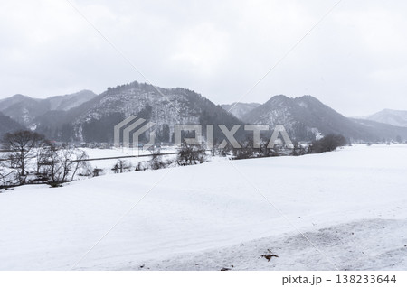 雪降る南会津の冬景色、一面の雪原と雪化粧した山並みが広がる里山の風景 138233644