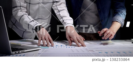 Collaboration of business professionals analyzing financial charts and data on papers and tablet, working late on a new strategy for company success Collaboration of business professionals analyzing financial charts and data on papers and tablet, working late on a new strategy for company success 138233864