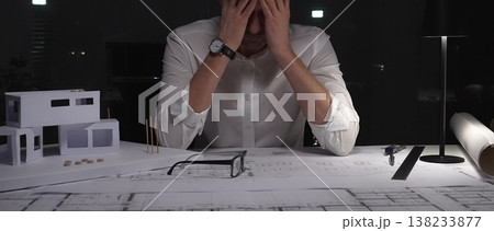 Architect experiencing burnout and stress, working late at night in a dark office with building models and blueprints. Architect experiencing burnout and stress, working late at night in a dark office with building models and blueprints. 138233877