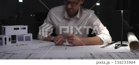 Architect working late on building plans and a residential house model, designing a new construction project. Business and architect people concept 138233984