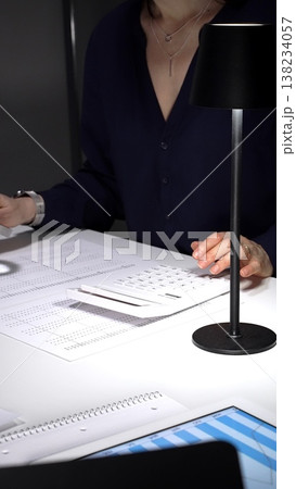Person checking financial documents and numbers with a magnifying glass, analyzing business data for budgeting and taxes at night. Audit and taxes in business Person checking financial documents and numbers with a magnifying glass, analyzing business data for budgeting and taxes at night. Audit and taxes in business 138234057