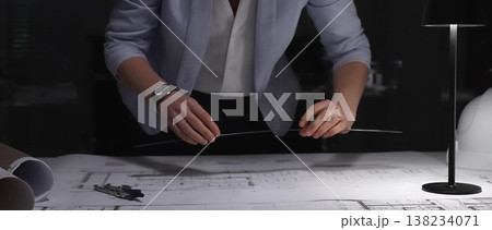 Architect hand drawing building plan, focused on engineering blueprints at office desk, hard hat nearby, late working hours 138234071