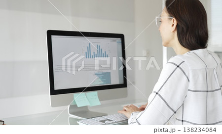 Businesswoman at glass office desk analyzing charts and graphs on computer screen, reviewing financial reports and performance data for planning. Business people concept Businesswoman at glass office desk analyzing charts and graphs on computer screen, reviewing financial reports and performance data for planning. Business people concept 138234084
