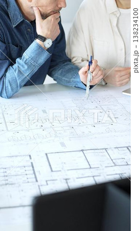 Engineering professionals collaborating on an architectural blueprint, using a compass to design a modern building, planning construction with a house model and laptop 138234100