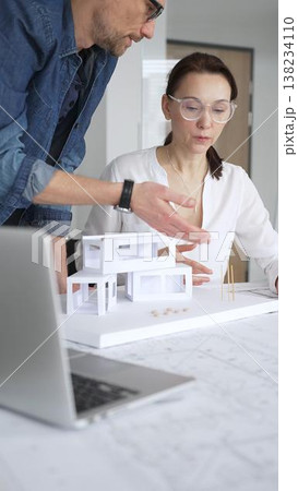 Architects collaborating on building design, a female showing a colleague a blueprint layout while creating a physical architectural model in an office 138234110