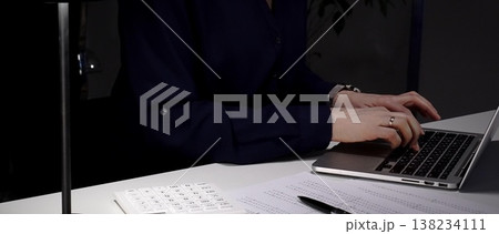 Woman's hands typing on laptop at office desk, working late night with calculator and financial documents. Audit and taxes in business 138234111