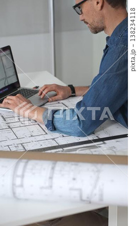 Architect hands reviewing building blueprints and housing plans on a table, utilizing a laptop for architectural drawing and design while planning a construction project Architect hands reviewing building blueprints and housing plans on a table, utilizing a laptop for architectural drawing and design while planning a construction project 138234118