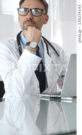 Male doctor wearing spectacles, thinking about healthcare diagnosis while using a laptop in a clinic office. Medicine and health care Male doctor wearing spectacles, thinking about healthcare diagnosis while using a laptop in a clinic office. Medicine and health care 138234143