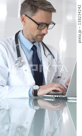 Male doctor in white coat with stethoscope, focused on laptop at reflective clinic desk, telemedicine consultation and research work. Medicine and health care Male doctor in white coat with stethoscope, focused on laptop at reflective clinic desk, telemedicine consultation and research work. Medicine and health care 138234242