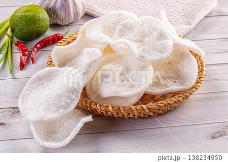 Crispy shrimp chips in a woven basket with fresh chili, lime, and garlic ingredients on a wooden table Crispy shrimp chips in a woven basket with fresh chili, lime, and garlic ingredients on a wooden table 138234950