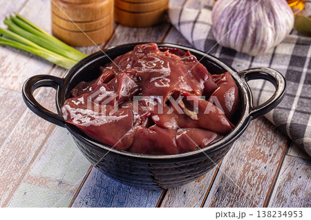 Raw chicken liver in a black bowl with garlic, chili, and spices on a rustic wooden table. 138234953