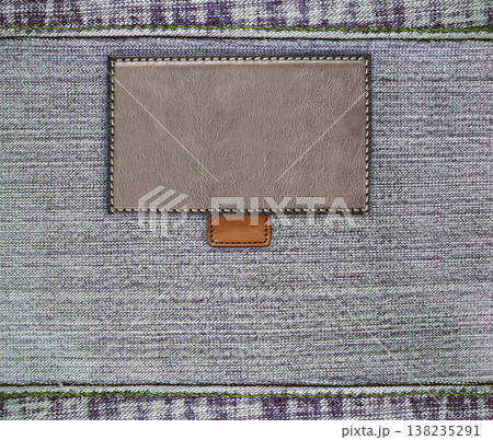 Gray denim texture with a seam and old leather label. Light grey color denim jeans material and vintage tag of brown color. Mock up template. Copy space for text Gray denim texture with a seam and old leather label. Light grey color denim jeans material and vintage tag of brown color. Mock up template. Copy space for text 138235291