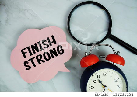 Finish Strong text with magnifying glass and alarm clock on marble background 138236152