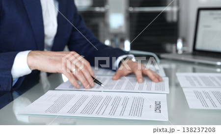 Business person reviewing a contract document, signing an agreement in an office setting, hands holding a pen, close up on the legal papers and corporate deal negotiations 138237208