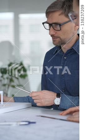 Architects collaborating on architectural plans. Designing modern building models. Drawing blueprints. Engineering innovative residential project solutions Architects collaborating on architectural plans. Designing modern building models. Drawing blueprints. Engineering innovative residential project solutions 138237209