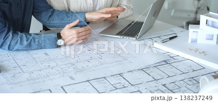 Architects engaging in a professional meeting, reviewing detailed blueprints on a table, utilizing a laptop, and collaborating on building design and construction planning Architects engaging in a professional meeting, reviewing detailed blueprints on a table, utilizing a laptop, and collaborating on building design and construction planning 138237249