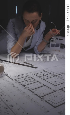 Architect woman experiencing stress and frustration from project deadline working late at night in office. Architecture and business concept in low key lighting Architect woman experiencing stress and frustration from project deadline working late at night in office. Architecture and business concept in low key lighting 138237541