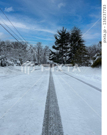 青空と雪に覆われた住宅街の道路に伸びるタイヤ跡 138237783