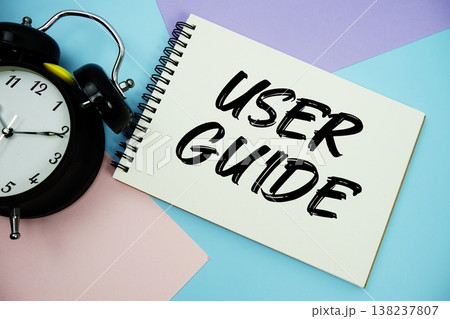 User Guide text written on notepad with alarm clock flat lay on multicolor pastel background 138237807