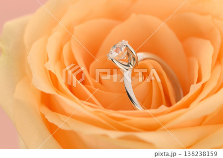 Ring with a central stone sits atop a soft orange rose, evoking romance 138238159