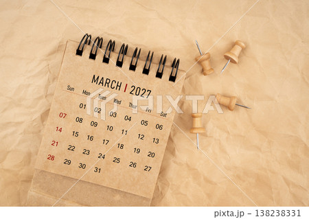 March 2027 desk calendar with wooden thumbtack on brown crumpled paper background. 138238331