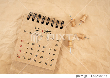 May 2027 desk calendar with wooden thumbtack on brown crumpled paper background. 138238333