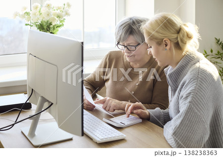 Senior woman with adult daughter paying bills online at home computer desk Senior woman with adult daughter paying bills online at home computer desk 138238363