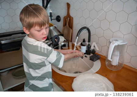 Child washes hands at kitchen sink during home baking preparation, everyday family cooking routine. Learning hygiene, child involvement, domestic lifestyle, home 138239361