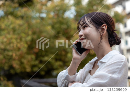 屋外の木のあるところで携帯電話で喋っている若い女性 屋外の木のあるところで携帯電話で喋っている若い女性 138239699