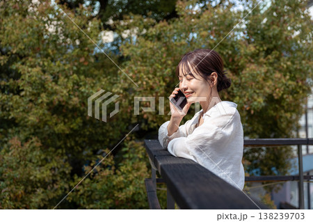 屋外の木のあるところで携帯電話で喋っている若い女性 138239703