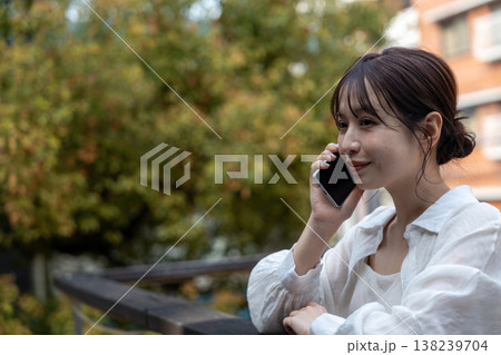 屋外の木のあるところで携帯電話で喋っている若い女性 138239704