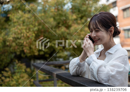 屋外の木のあるところで携帯電話で喋っている若い女性 138239706