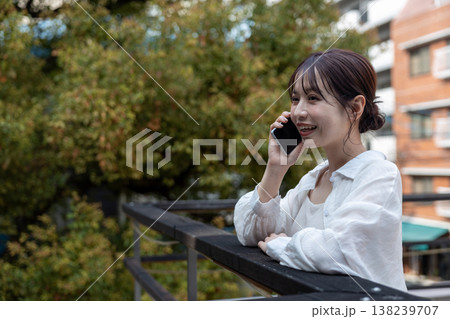 屋外の木のあるところで携帯電話で喋っている若い女性 138239707