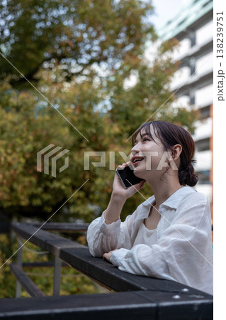 屋外の木のあるところで携帯電話で喋っている若い女性 屋外の木のあるところで携帯電話で喋っている若い女性 138239751