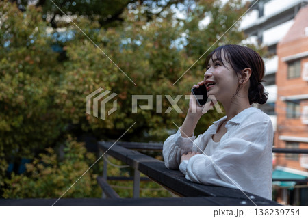 屋外の木のあるところで携帯電話で喋っている若い女性 138239754