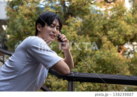 木のあるところで携帯電話で喋っている若い男性 138239887