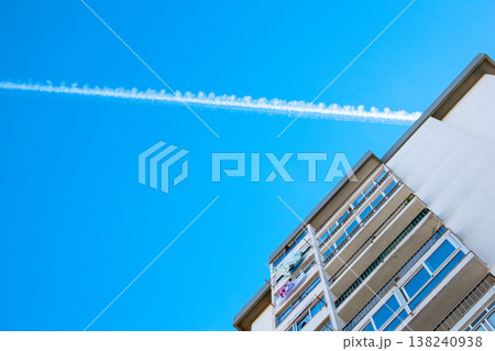Airplane Vapor Trail in Sunny Sky Between Contemporary Urban Architecture Airplane Vapor Trail in Sunny Sky Between Contemporary Urban Architecture 138240938