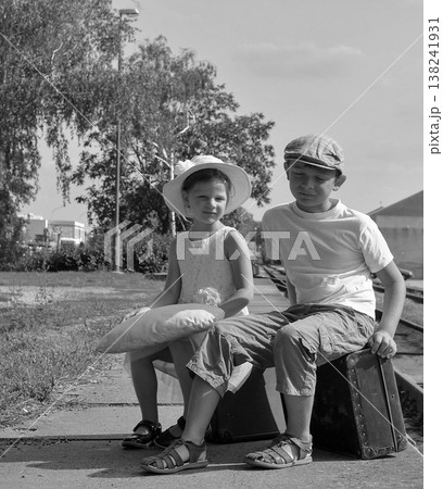Two children in vintage clothing wait on a train platform with luggage Two children in vintage clothing wait on a train platform with luggage 138241931