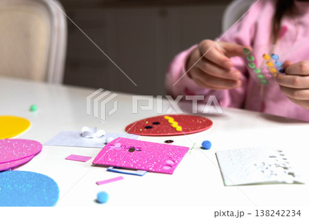 Child hands making festive easter egg craft with glue and foam shapes. 138242234