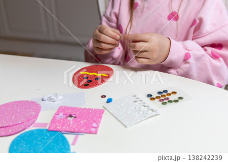 Child hands making festive easter egg craft with glue and foam shapes. Child hands making festive easter egg craft with glue and foam shapes. 138242239