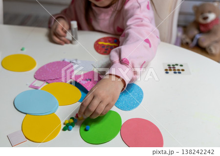 Child hands making festive easter egg craft with glue and foam shapes. 138242242