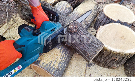 Hand holds chain saw with battery to trim broken branch of an tree. Modern work with electric portable brushless cordless chain saw. Hand holds chain saw with battery to trim broken branch of an tree. Modern work with electric portable brushless cordless chain saw. 138243253